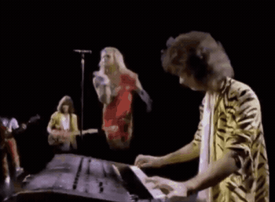 A Man In A Tiger Print Shirt Is Playing A Keyboard In Front Of A Group Of Musicians . GIF