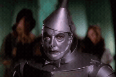 A Man In A Tin Man Costume From The Wizard Of Oz Is Standing In Front Of A Crowd Of People . GIF