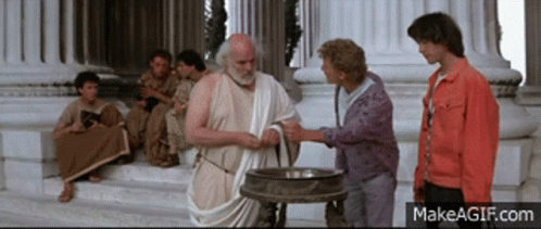 A Man In A Toga Shakes Hands With Another Man In Front Of A Group Of People GIF