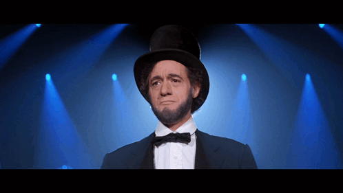 A Man In A Top Hat And Bow Tie Is Standing In Front Of Blue Lights GIF