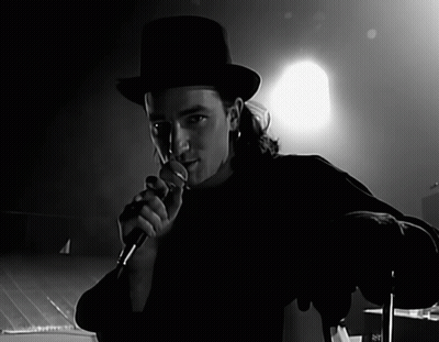 A Man In A Top Hat Is Singing Into A Microphone In A Black And White Photo GIF