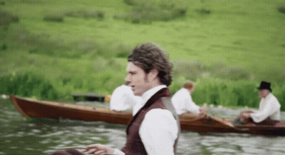 A Man In A Top Hat Sits In A Boat On A Lake GIF