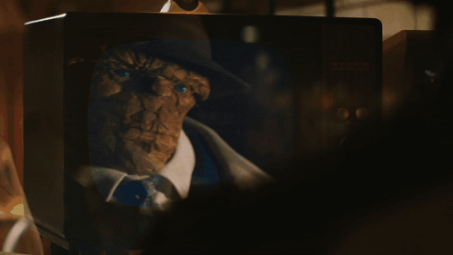 A Man In A Trench Coat And Hat Is Walking Down A Dark Street GIF