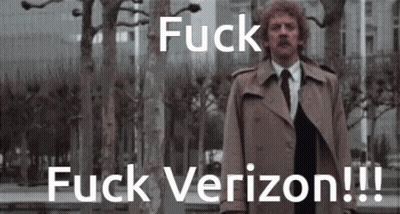 A Man In A Trench Coat And Tie Stands In Front Of Trees And Says Fuck Verizon !!! GIF