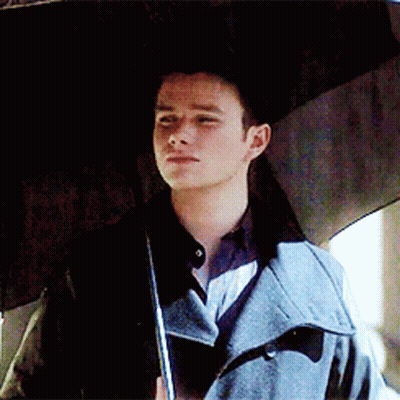 A Man In A Trench Coat Holds An Umbrella Over His Head GIF