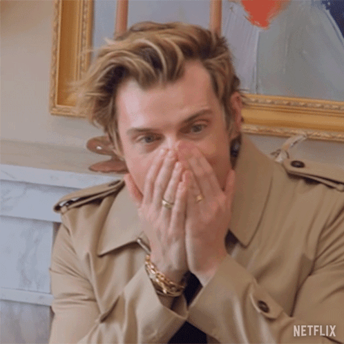 A Man In A Trench Coat Is Covering His Mouth With His Hands And A Netflix Logo Can Be Seen Behind Him GIF