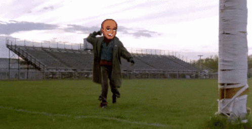 A Man In A Trench Coat Is Walking Across A Field GIF