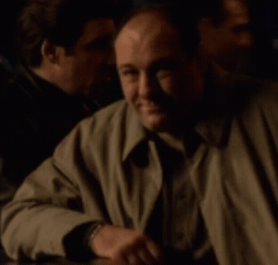 A Man In A Trench Coat Sits At A Table With Other Men GIF
