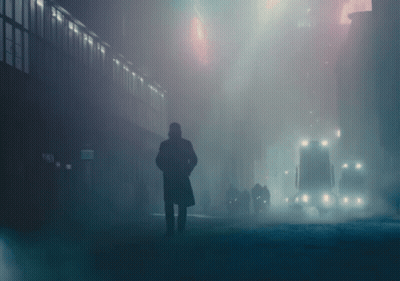 A Man In A Trench Coat Stands In A Foggy City Street GIF