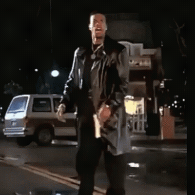 A Man In A Trench Coat Stands On A Street At Night GIF