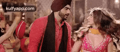 A Man In A Turban Is Standing Next To A Woman In A Pink Dress And Talking To Her . GIF