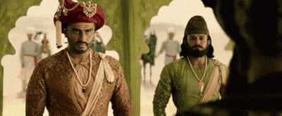 A Man In A Turban Is Standing Next To Another Man In A Costume . GIF