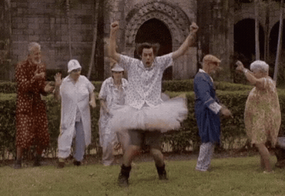 A Man In A Tutu Is Dancing With A Group Of Elderly People In A Park . GIF