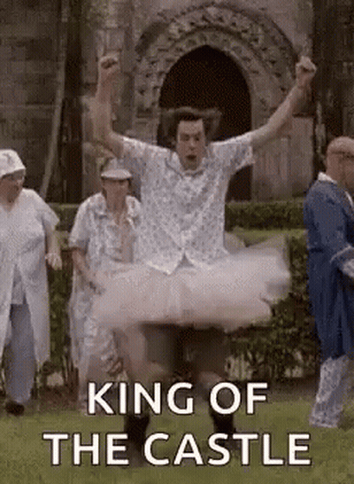 A Man In A Tutu Is Jumping In The Air In Front Of A Castle . GIF