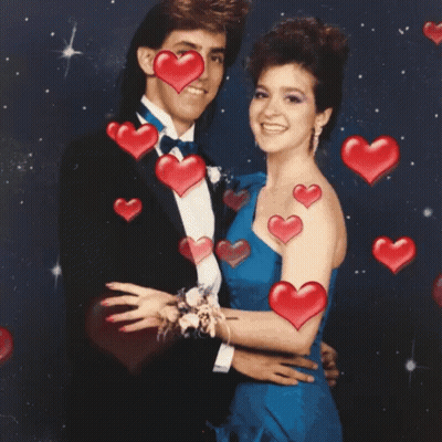 A Man In A Tuxedo And A Woman In A Blue Dress Are Posing For A Picture With Red Hearts Surrounding Them GIF