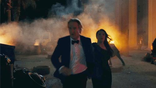 A Man In A Tuxedo And A Woman In A Blue Dress Are Running From A Fire GIF