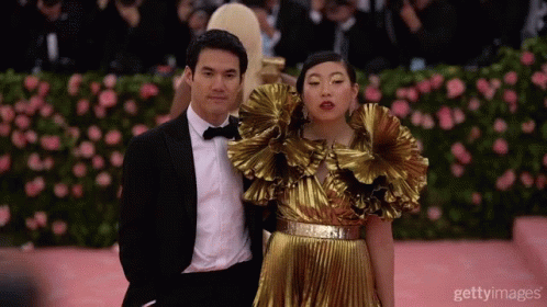 A Man In A Tuxedo And A Woman In A Gold Dress Pose For A Photo GIF