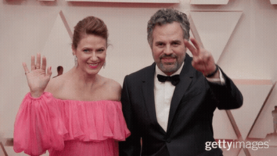 A Man In A Tuxedo And A Woman In A Pink Dress Are Standing Next To Each Other GIF