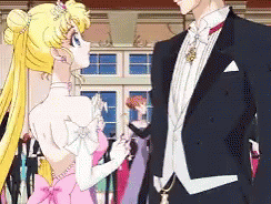 A Man In A Tuxedo And A Woman In A Pink Dress Are Standing Next To Each Other GIF