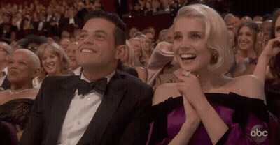 A Man In A Tuxedo And A Woman In A Purple Dress Are Sitting In The Audience At An Abc Awards Show GIF