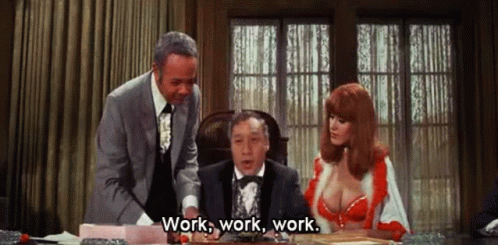 A Man In A Tuxedo And A Woman In A Red Bra Are Sitting At A Desk And Talking To Each Other . GIF