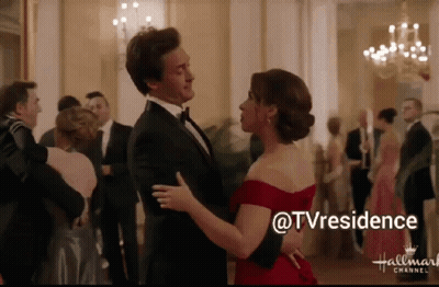 A Man In A Tuxedo And A Woman In A Red Dress Are Dancing In Front Of A Hallmark Channel Logo GIF