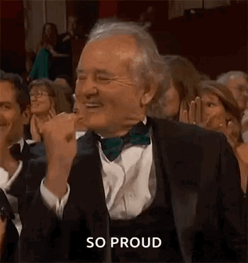 A Man In A Tuxedo And Bow Tie Is Applauding In A Crowd Of People . GIF