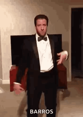 A Man In A Tuxedo And Bow Tie Is Dancing In Front Of A Television . GIF