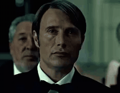 A Man In A Tuxedo And Bow Tie Is Looking At The Camera With Two Men Behind Him . GIF
