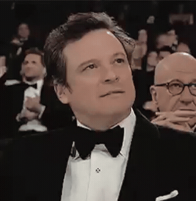 A Man In A Tuxedo And Bow Tie Is Sitting In Front Of A Crowd . GIF