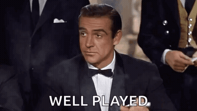 A Man In A Tuxedo And Bow Tie Is Sitting In Front Of A Group Of Men And Saying `` Well Played '' . GIF