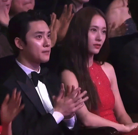 A Man In A Tuxedo And Bow Tie Is Sitting Next To A Woman In A Red Dress Who Is Clapping Her Hands . GIF