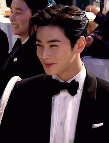 A Man In A Tuxedo And Bow Tie Is Smiling While Sitting At A Table GIF