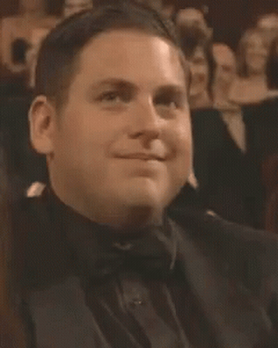 A Man In A Tuxedo And Bow Tie Is Smiling While Sitting In A Theatre . GIF