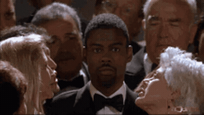 A Man In A Tuxedo And Bow Tie Is Standing In A Crowd Of People GIF