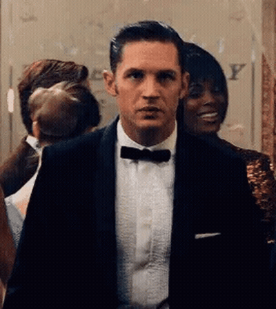 A Man In A Tuxedo And Bow Tie Is Standing In A Room With Other People . GIF
