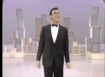 A Man In A Tuxedo And Bow Tie Is Walking On A Stage GIF