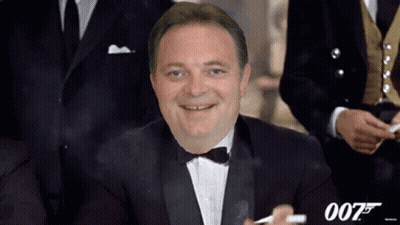A Man In A Tuxedo And Bow Tie Smoking A Cigarette With The Number 007 Behind Him GIF
