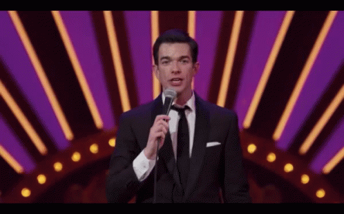 A Man In A Tuxedo And Tie Is Holding A Microphone GIF