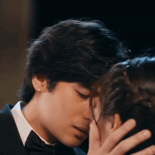 A Man In A Tuxedo And Tie Is Kissing A Woman On The Cheek . GIF