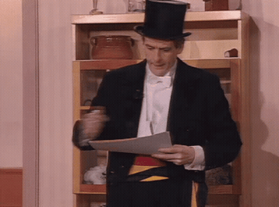 A Man In A Tuxedo And Top Hat Holds A Piece Of Paper GIF
