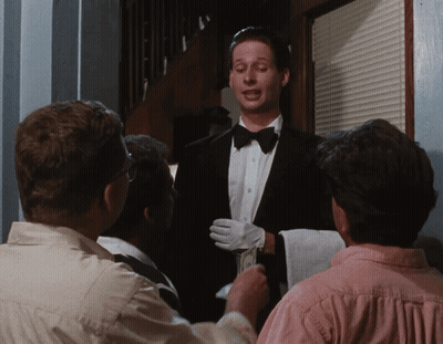 A Man In A Tuxedo And White Gloves Is Talking To A Group Of People GIF