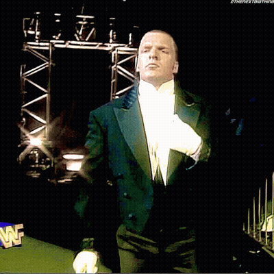 A Man In A Tuxedo And White Gloves Stands In Front Of A Wwe Logo GIF