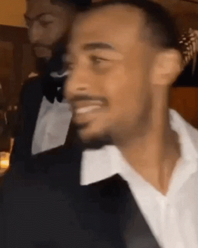 A Man In A Tuxedo And White Shirt Is Smiling At A Party . GIF