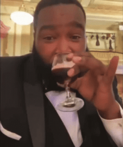 A Man In A Tuxedo Drinking A Glass Of Wine GIF