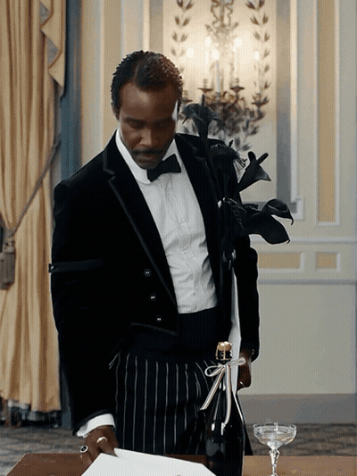 A Man In A Tuxedo Holds A Bottle Of Champagne With A Bow On It GIF