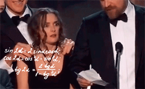 A Man In A Tuxedo Holds A Piece Of Paper In Front Of A Microphone While A Woman Stands Behind Him GIF