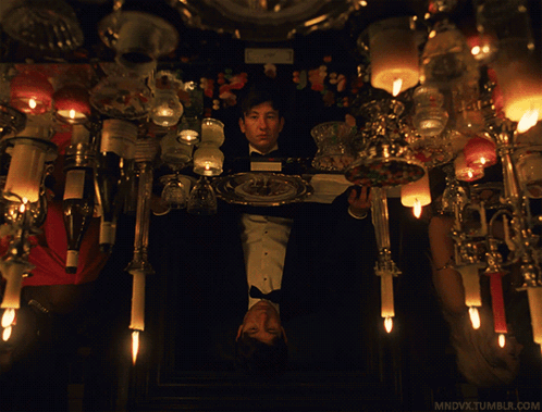 A Man In A Tuxedo Holds A Plate With A Candle On It In Front Of Candles GIF