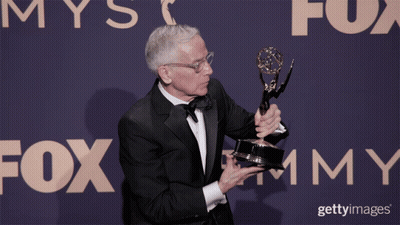 A Man In A Tuxedo Holds A Trophy In Front Of A Fox Advertisement GIF