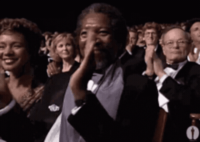 A Man In A Tuxedo Is Clapping His Hands In A Crowd Of People . GIF